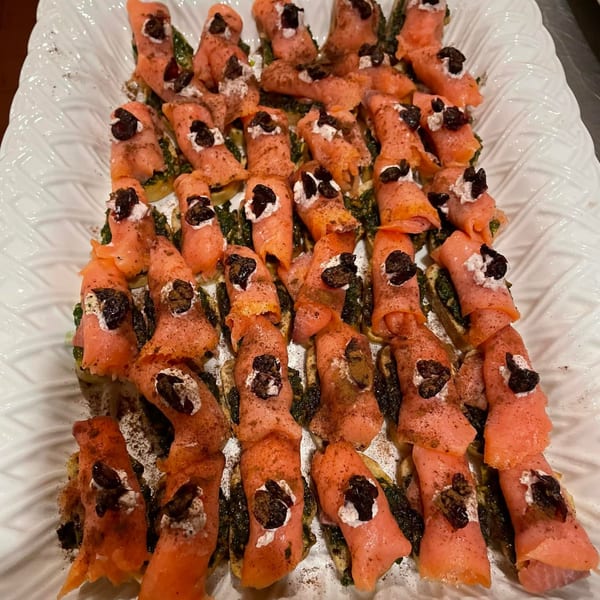 Close-up of salmon rolls with cream cheese and olives on a white textured platter.