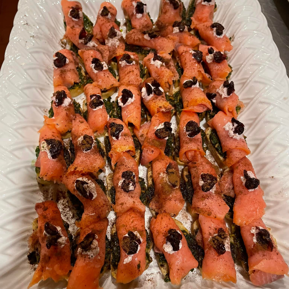Close-up of salmon rolls with cream cheese and olives on a white textured platter.