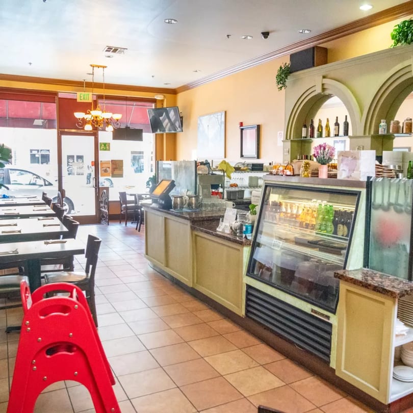 Interior of Sage Bistro with empty tables, a service counter, and a refrigerated display case.