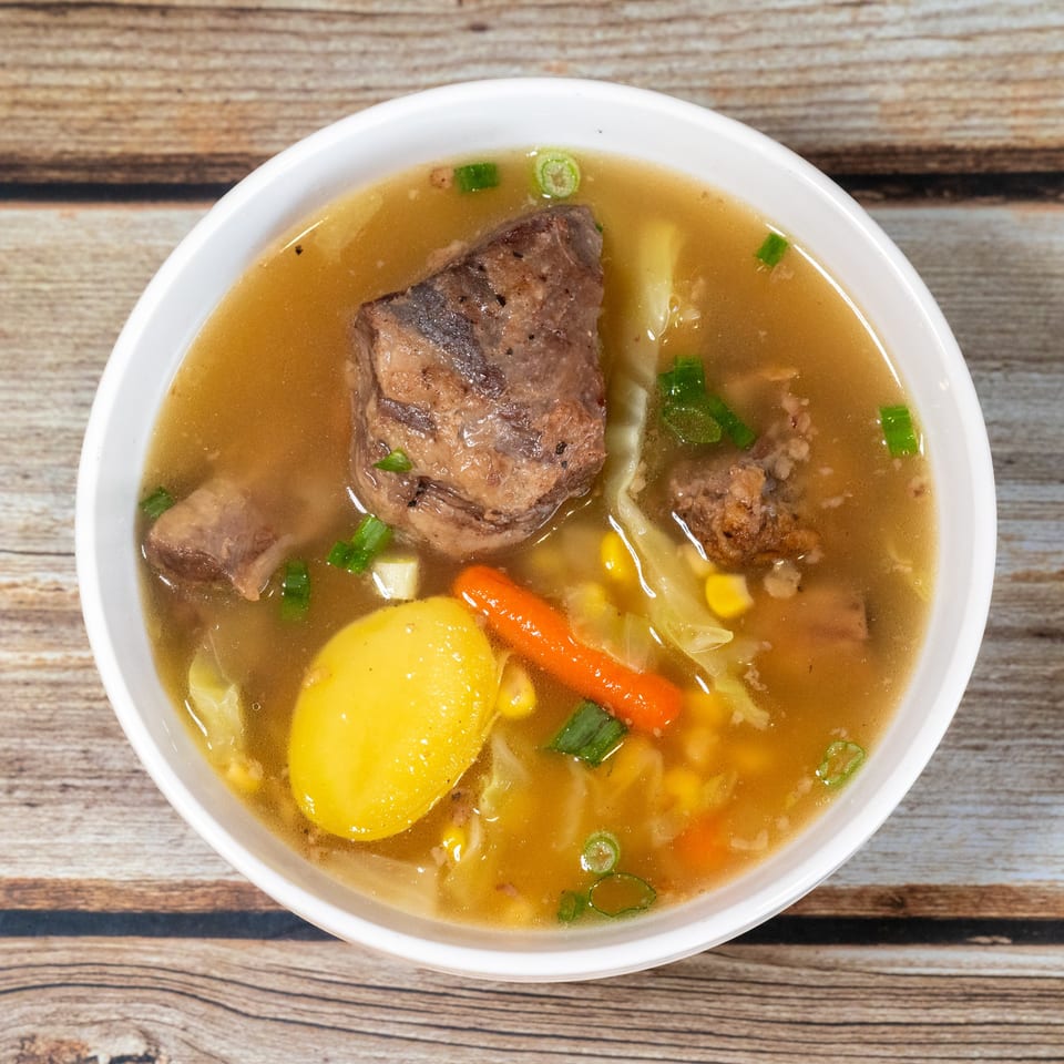 Hearty beef stew with potatoes, carrots, corn, and cabbage in a white bowl.