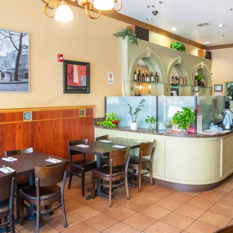 Interior of Sage Bistro with empty tables, a service counter, and decorative plants.