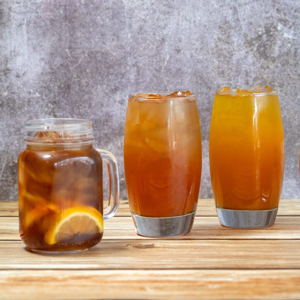 Three iced tea drinks, one with a lemon slice, on a wooden table at Sage Bistro.