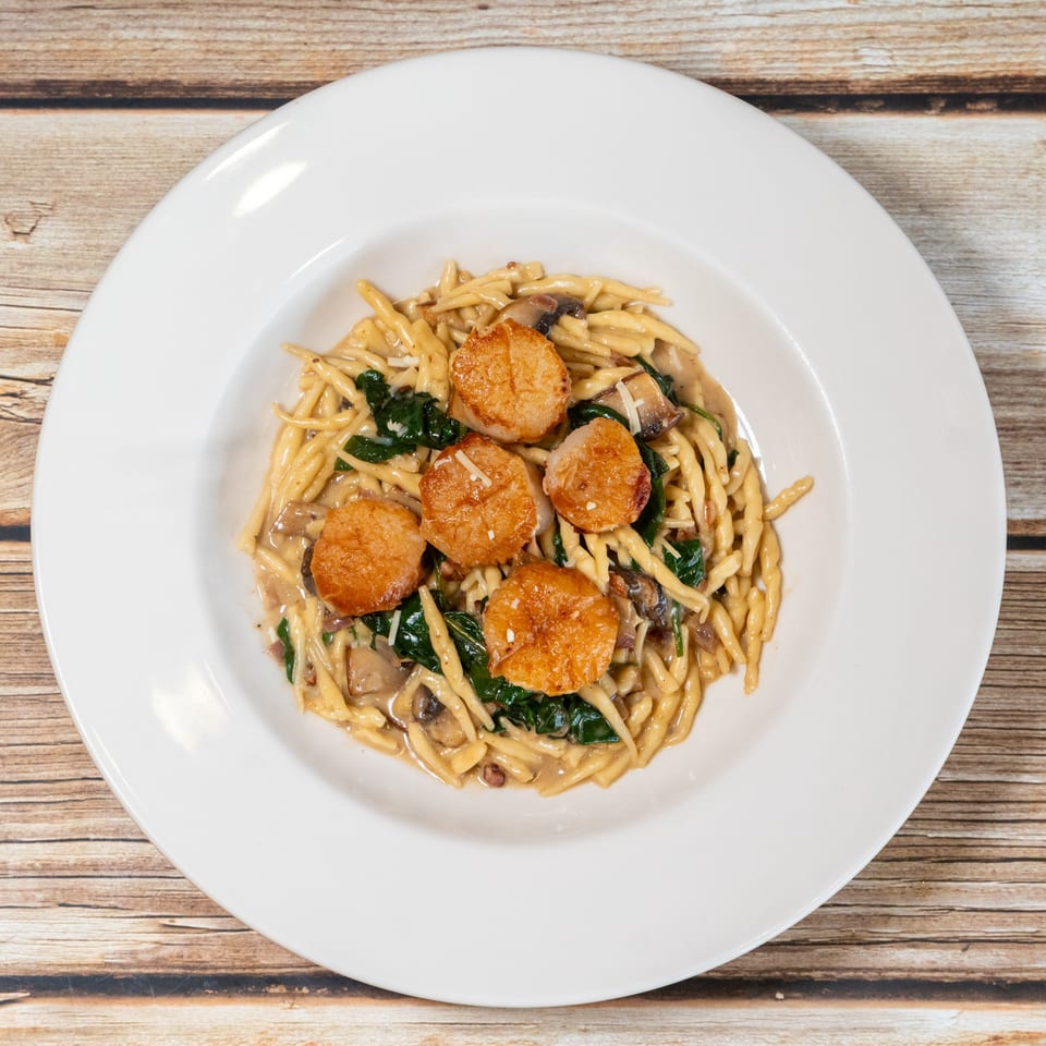 Sage Bistro's scallops with pasta, spinach, and mushrooms in a creamy sauce, topped with cheese.