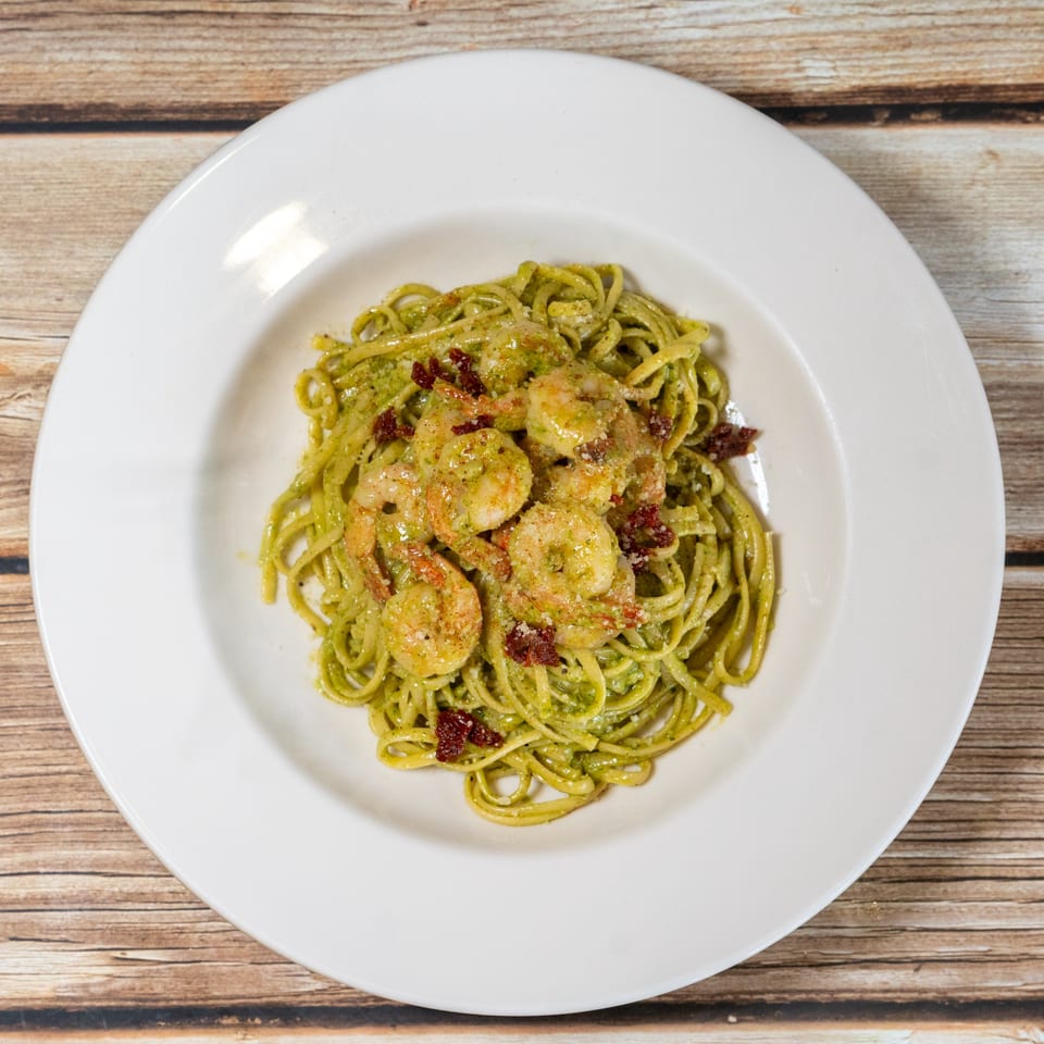 Sage Bistro's pesto linguine with shrimp and sun-dried tomatoes in a white bowl on wood.