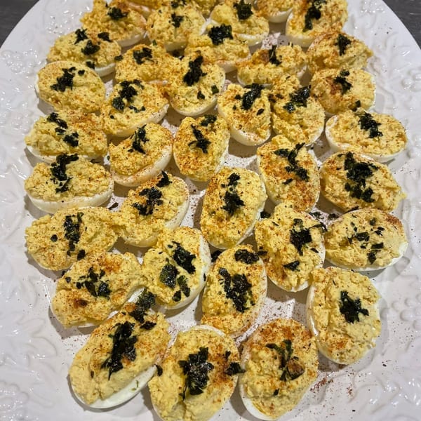 A white platter filled with deviled eggs, garnished with paprika and dark green herbs.