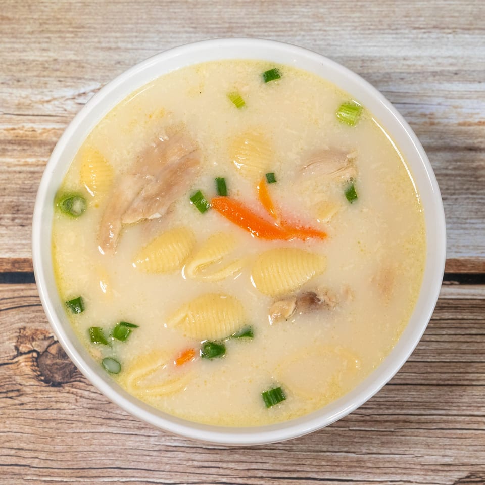 Creamy chicken noodle soup with shell pasta, carrots, and green onions in a white bowl.